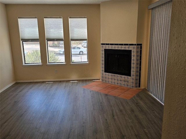 unfurnished living room featuring a tiled fireplace, baseboards, and wood finished floors