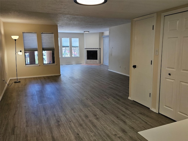 unfurnished living room featuring baseboards, a brick fireplace, dark wood-style flooring, and a textured ceiling