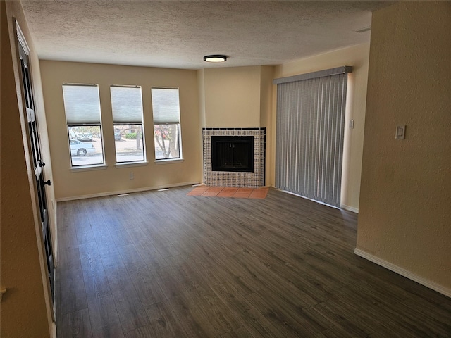 unfurnished living room with a textured ceiling, dark wood finished floors, a tile fireplace, baseboards, and a textured wall