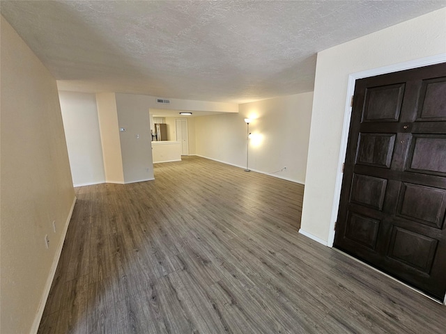 unfurnished living room featuring a textured ceiling, baseboards, visible vents, and wood finished floors