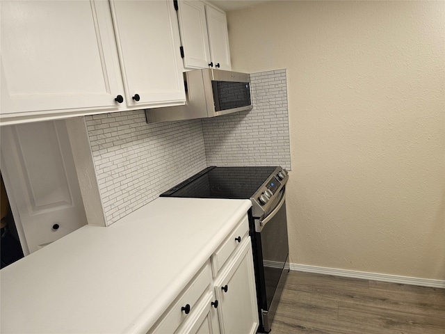 kitchen featuring white cabinets, light countertops, baseboards, dark wood-type flooring, and range with electric stovetop
