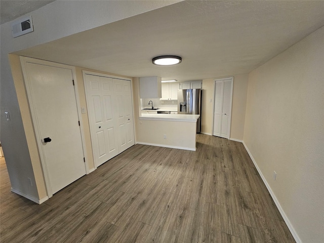 unfurnished living room with baseboards, a sink, and dark wood-style flooring