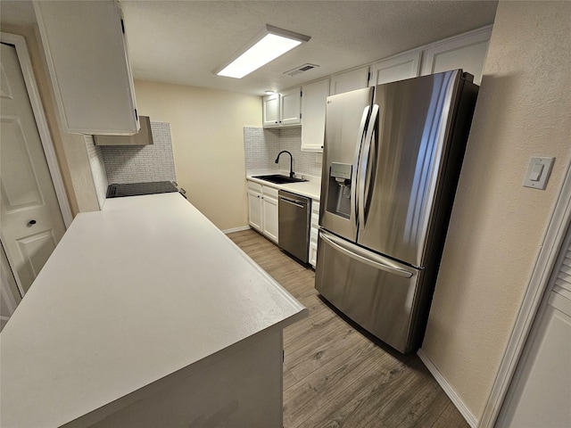 kitchen with decorative backsplash, light countertops, a sink, light wood finished floors, and stainless steel appliances