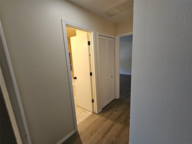 corridor with a textured wall, visible vents, and wood finished floors