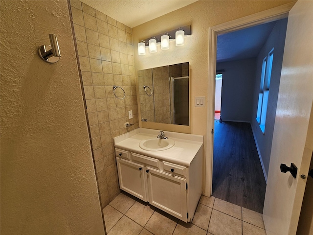 full bath with tile patterned flooring, a textured wall, vanity, and tiled shower