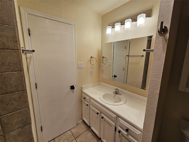 bathroom with toilet, a textured wall, tile patterned flooring, and vanity