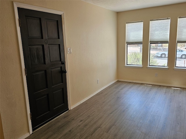 spare room with baseboards, a textured wall, and dark wood-type flooring