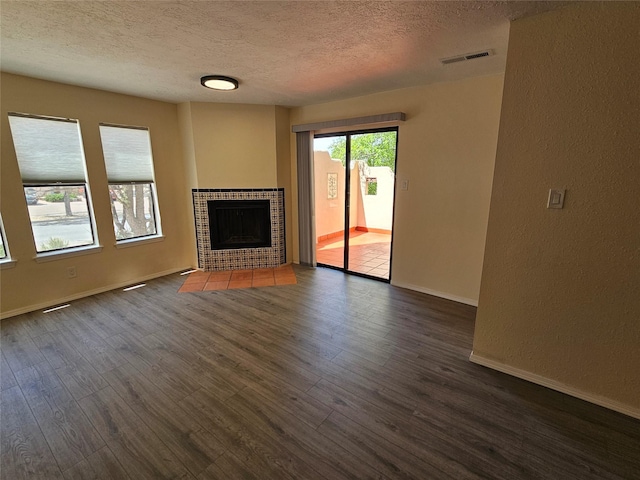 unfurnished living room with visible vents, a textured ceiling, dark wood-type flooring, and a fireplace