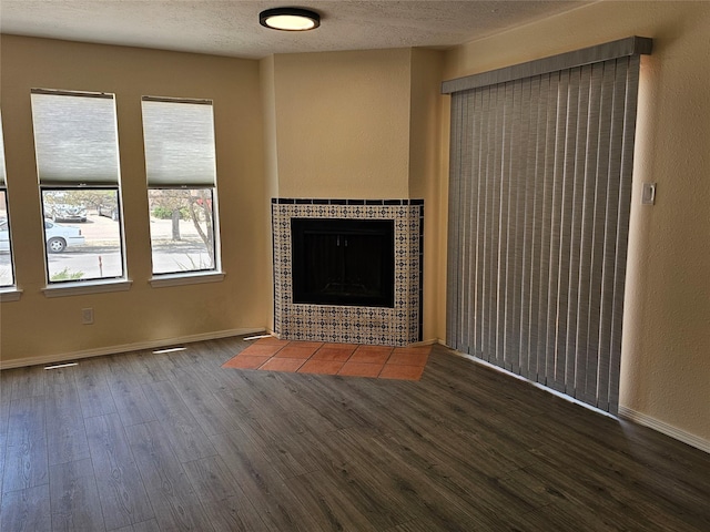 unfurnished living room with a textured ceiling, baseboards, wood finished floors, and a tile fireplace