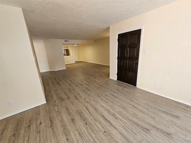 unfurnished room featuring baseboards, visible vents, a textured ceiling, and wood finished floors