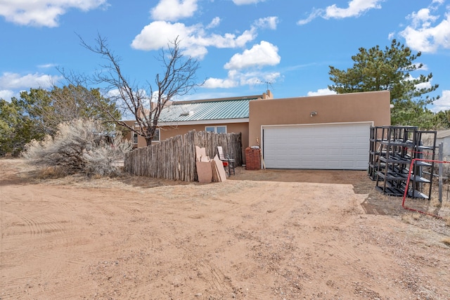 exterior space featuring driveway, metal roof, a garage, fence, and stucco siding