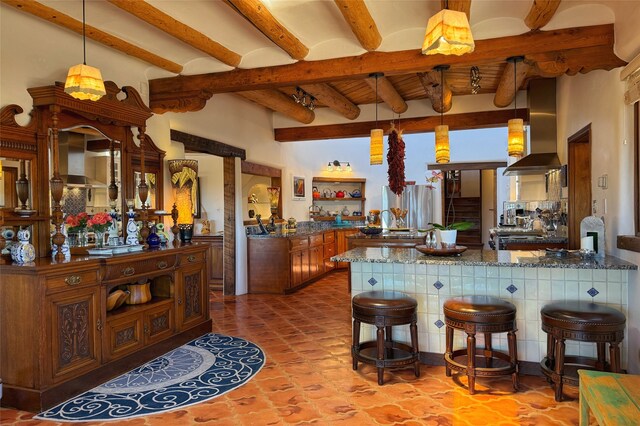 kitchen featuring a peninsula, beamed ceiling, pendant lighting, and wall chimney exhaust hood