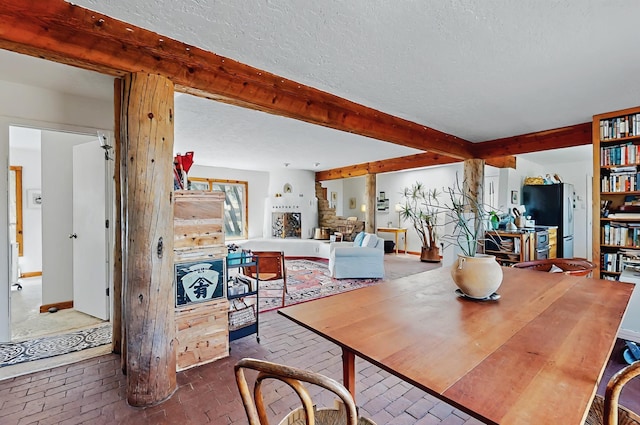 dining space with a textured ceiling, brick floor, and beamed ceiling