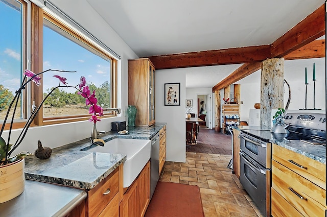 kitchen featuring beam ceiling, brick floor, a sink, dark stone countertops, and stainless steel appliances