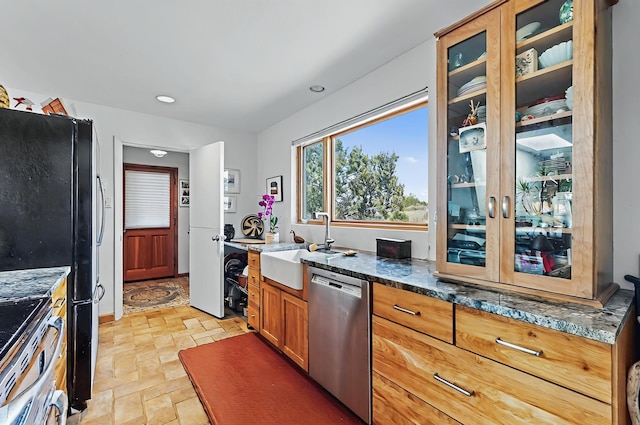 kitchen featuring brown cabinets, a sink, glass insert cabinets, dark stone counters, and stainless steel appliances