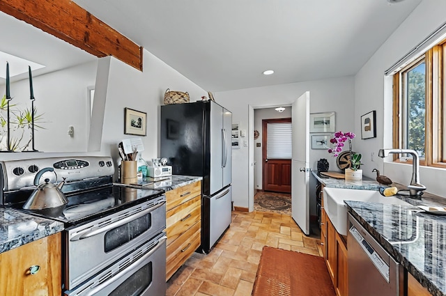kitchen featuring a sink, dark stone counters, stainless steel appliances, recessed lighting, and stone finish flooring
