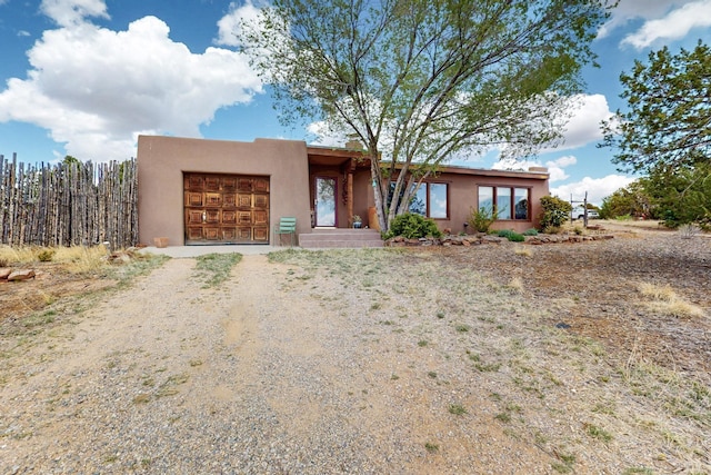 pueblo-style home with an attached garage, driveway, and stucco siding