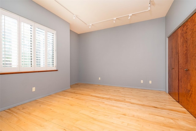 unfurnished bedroom with multiple windows, a closet, rail lighting, and wood finished floors