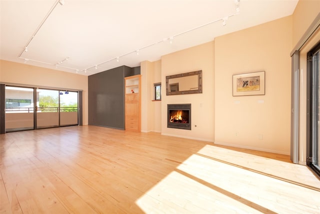 unfurnished living room with light wood finished floors, rail lighting, and a warm lit fireplace