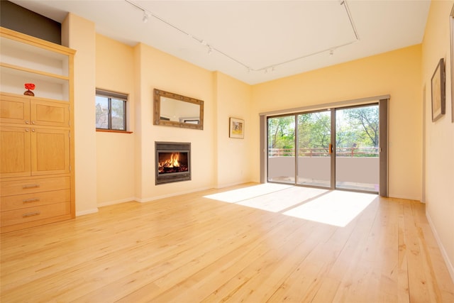 unfurnished living room with track lighting, light wood finished floors, baseboards, and a lit fireplace
