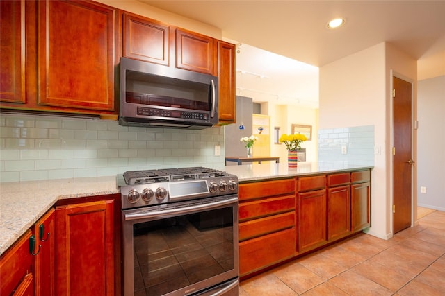 kitchen featuring light stone counters, stainless steel appliances, light tile patterned floors, reddish brown cabinets, and backsplash