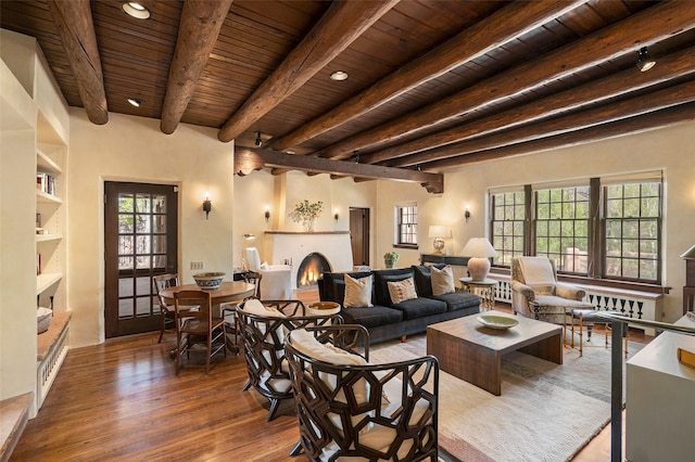 living room featuring wooden ceiling, beamed ceiling, a warm lit fireplace, and wood finished floors
