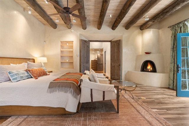 bedroom with wooden ceiling, beam ceiling, a large fireplace, and wood finished floors