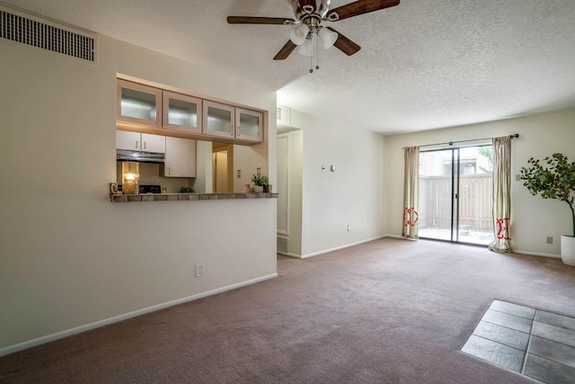 unfurnished living room with a ceiling fan, a textured ceiling, visible vents, carpet floors, and baseboards
