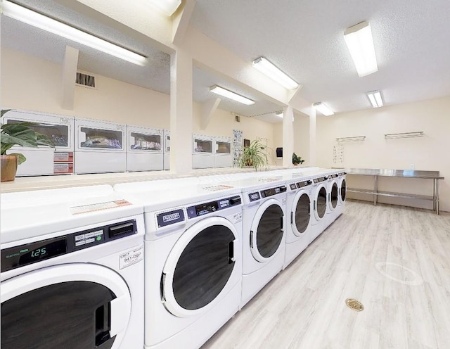 shared laundry area featuring visible vents, light wood finished floors, a textured ceiling, and washer and clothes dryer