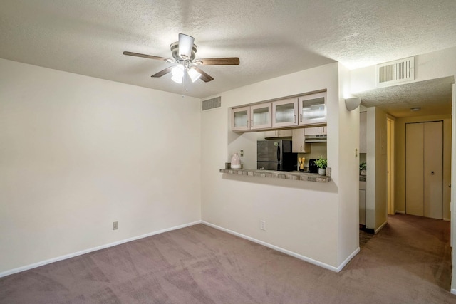 unfurnished living room with ceiling fan, carpet, a textured ceiling, and visible vents