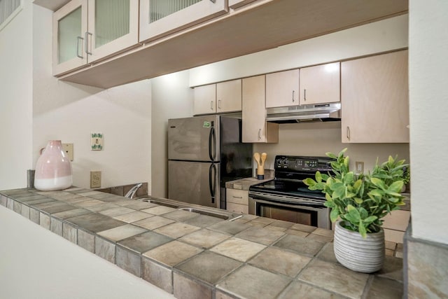 kitchen featuring glass insert cabinets, tile countertops, under cabinet range hood, a sink, and stainless steel appliances