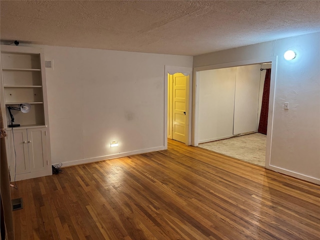 unfurnished bedroom with a textured ceiling, baseboards, visible vents, hardwood / wood-style flooring, and a closet