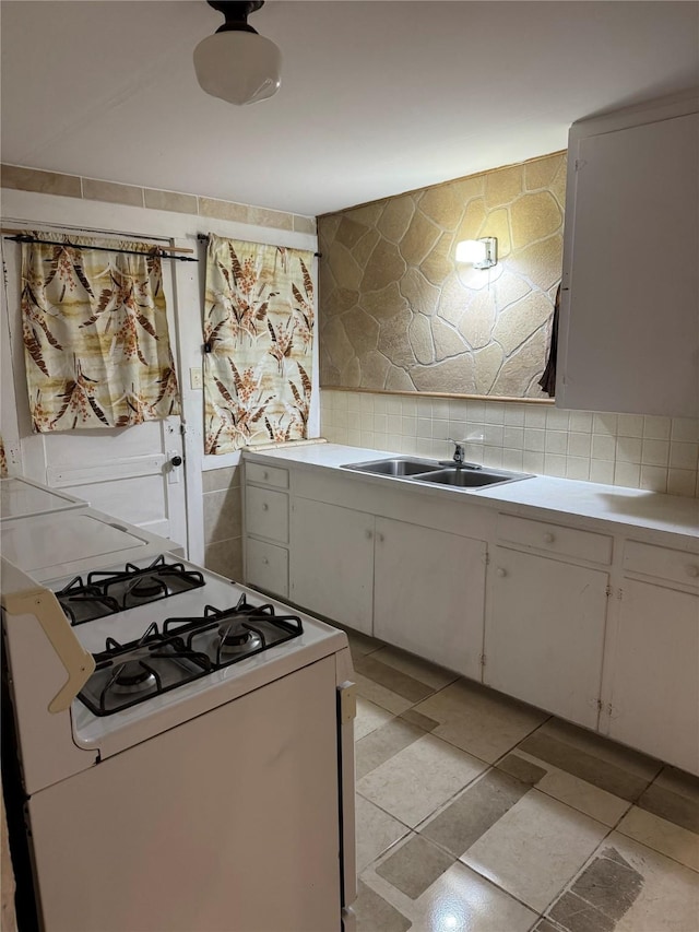 kitchen with decorative backsplash, a sink, light countertops, white range with gas stovetop, and white cabinetry