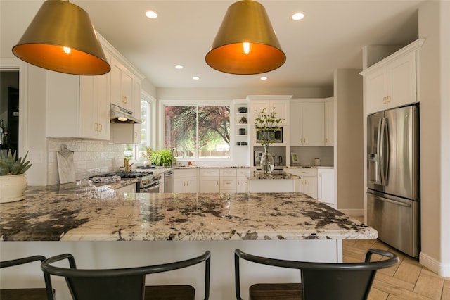 kitchen featuring a peninsula, stainless steel appliances, a kitchen breakfast bar, light stone countertops, and under cabinet range hood
