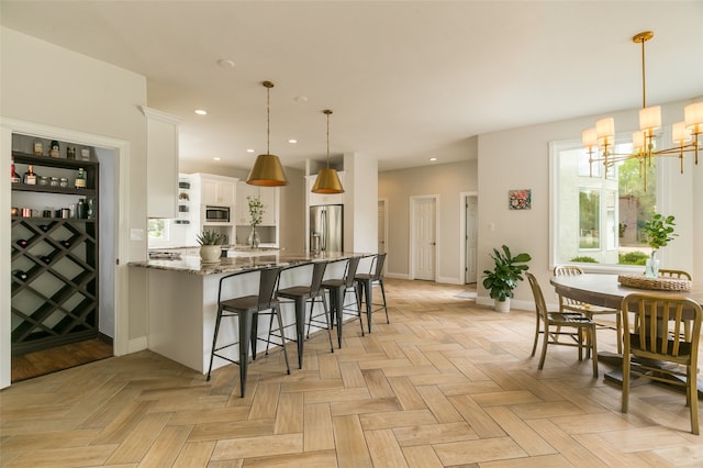 kitchen with stainless steel appliances, a breakfast bar, a chandelier, white cabinetry, and stone counters