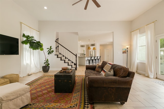 living area featuring ceiling fan, stairs, and baseboards