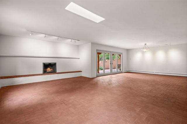 unfurnished living room with a baseboard radiator, rail lighting, a warm lit fireplace, and brick flooring