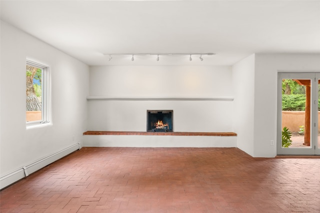 unfurnished living room with a baseboard radiator, track lighting, brick floors, and plenty of natural light