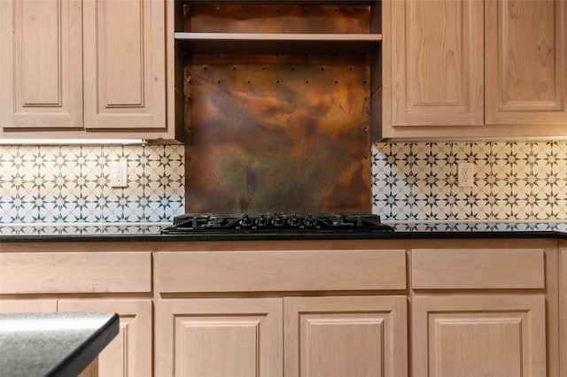 kitchen view of light brown cabinetry, backsplash, dark countertops, and black gas stovetop