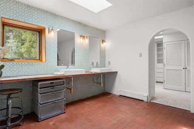 full bath featuring a baseboard radiator, a skylight, wallpapered walls, double vanity, and brick patterned flooring