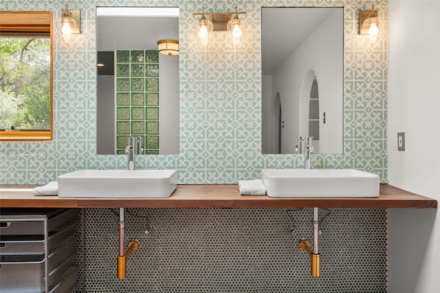 bathroom with dual sinks and wallpapered walls