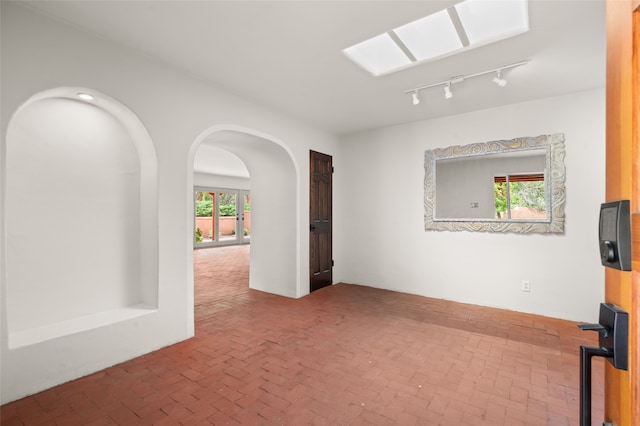 unfurnished room featuring brick floors, track lighting, and arched walkways