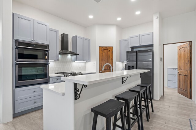 35 La Pradera, Santa Fe, NM 87508 - kitchen with wall chimney range hood, appliances with stainless steel finishes, light countertops, backsplash, and a kitchen breakfast bar