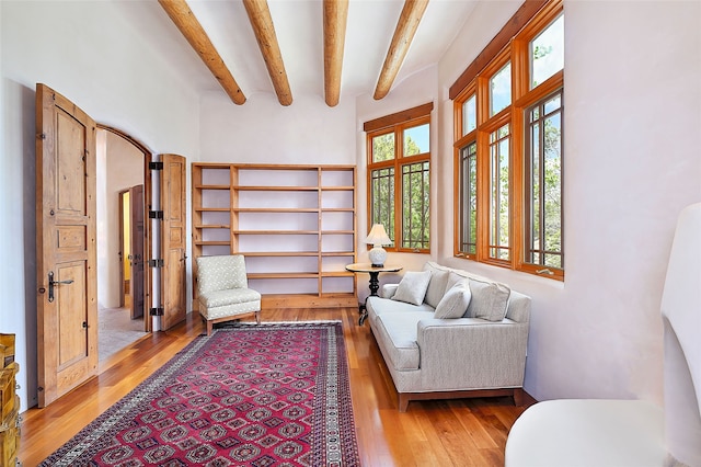 sitting room featuring wood-type flooring, beam ceiling, and a towering ceiling