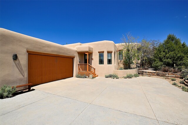 pueblo revival-style home with concrete driveway, a garage, and stucco siding