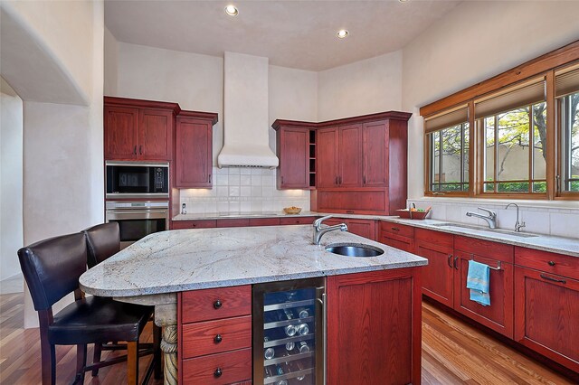 kitchen with a sink, beverage cooler, oven, built in microwave, and custom range hood