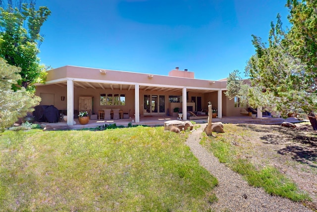 rear view of house with a chimney, a patio, and stucco siding