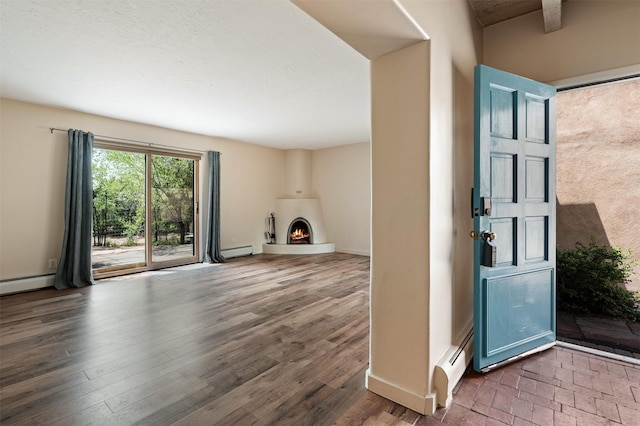 928 Los Lovatos Rd, Santa Fe, NM 87501 - entrance foyer featuring a baseboard radiator, baseboard heating, a lit fireplace, wood finished floors, and baseboards
