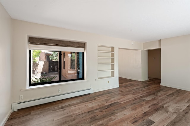 928 Los Lovatos Rd, Santa Fe, NM 87501 - empty room featuring a baseboard heating unit, built in shelves, wood finished floors, and baseboards