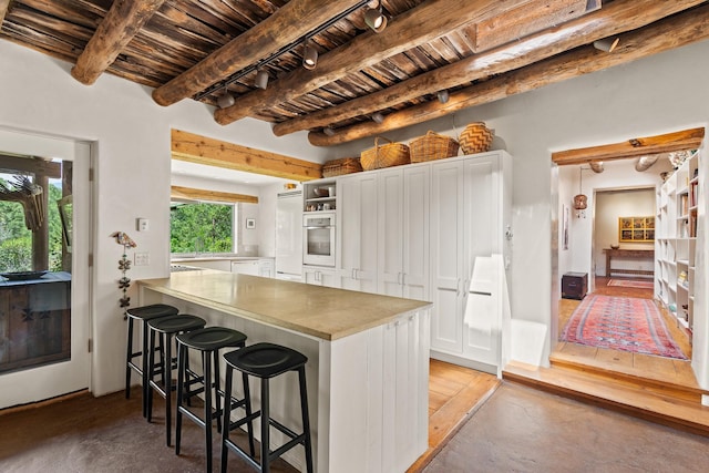 127 County Road 84, Santa Fe, NM 87506 - kitchen featuring stainless steel oven, wooden ceiling, beamed ceiling, a kitchen breakfast bar, and white cabinetry